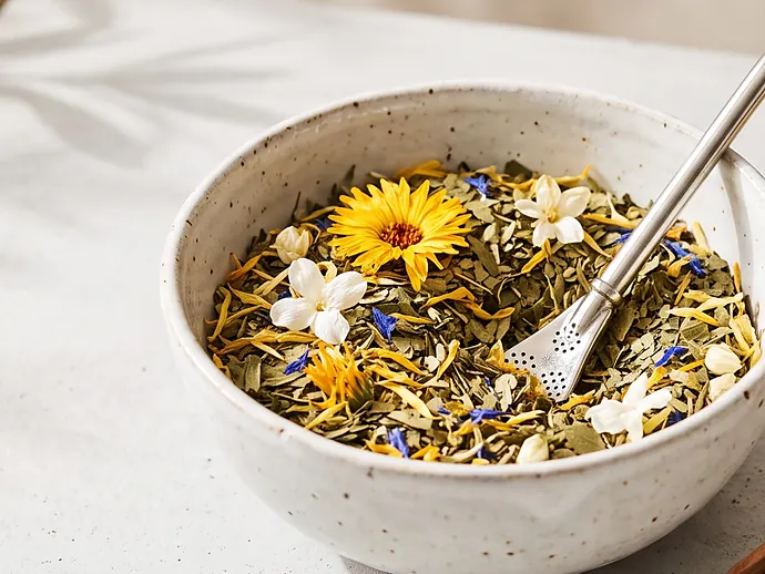 Bol de cerámica con un blend de hierbas y flores amarillas, con una bombilla de metal apoyada encima.